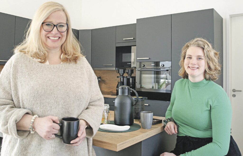 Zwei Frauen beim Kaffeetrinken in der Küche, lächeln in die Kamera